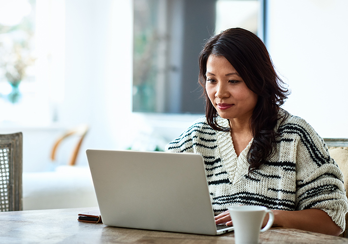 Mid adult woman in her 30s sitting at table and looking at computer, remote working, freelancer, small business