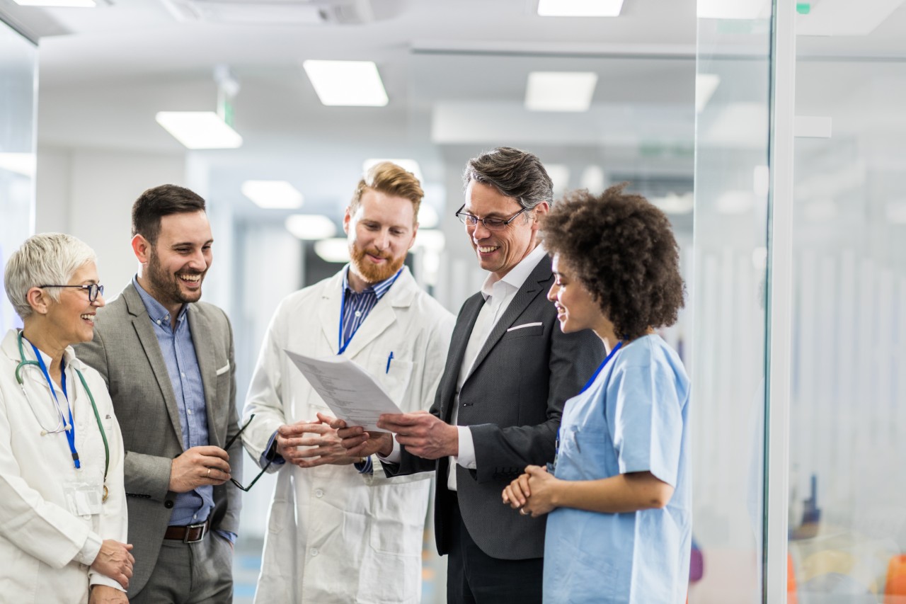 Team of happy doctors and two businessmen cooperating while going through paperwork in a hospital.
