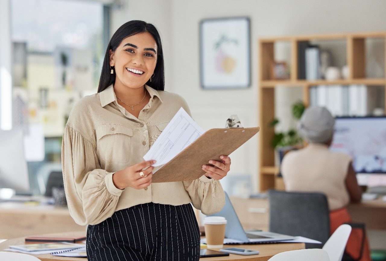 Review, contract and report with a business woman holding a clipboard with paperwork in her office at work. Application, document and proposal with a young female employee reading notes and working.